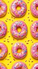 Pink donuts with various toppings like sprinkles and icing arranged in a fun, repeating design on a bright yellow background.