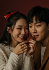 A young Asian couple smiles while enjoying a piece of shared chocolate with dark background
