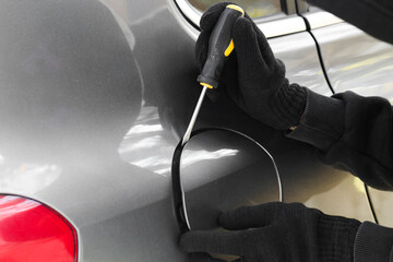 Thief with screwdriver opening fuel cap, closeup. Car hijacking