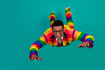 Young man wearing rainbow suit posing against a teal background, expressing joy and individuality