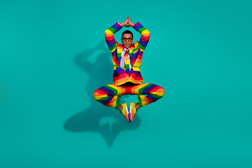 Charismatic young man in vibrant rainbow suit posing dynamically against teal background