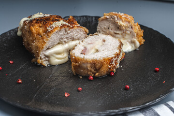Pieces of chicken cutlet Cordon Bleu with bacon and cheese according to a traditional French recipe on a black mica plate. Space for text.