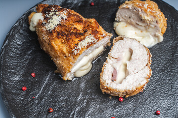 Pieces of chicken cutlet Cordon Bleu with bacon and cheese according to a traditional French recipe on a black mica plate. Space for text.