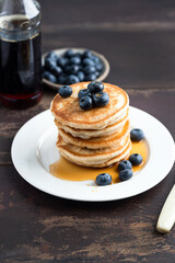 Stack of pancakes with blueberries and syrup on a wooden table background