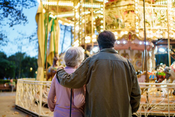 Fototapeta premium Elderly couple embracing and admiring carousel lights at dusk