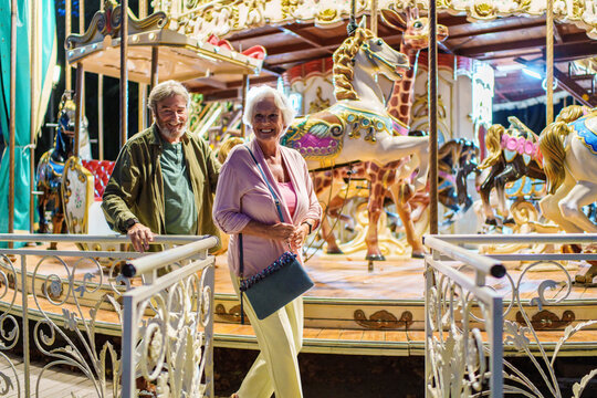 Happy senior couple exiting carousel at amusement park