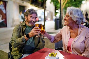 Happy senior couple toasting with beer at outdoor pub