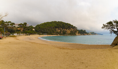 Panorámica de la Playa de Fenals en Catalunya, España, con arena dorada, mar y colinas verdes.