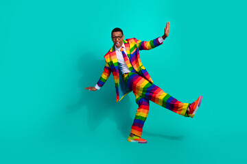 Colorful young man in a rainbow-striped suit posing against a turquoise background expressing fun and individuality