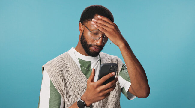 Phone, scam or black man with stress reading for bad news, password error or online crisis in studio. Anxiety, hacked or frustrated person by blue background for loss, digital fraud or notification