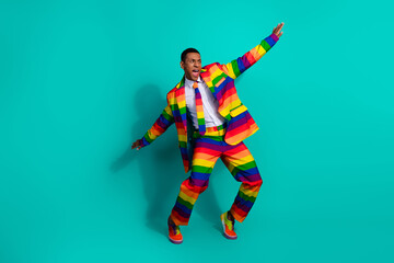 Dynamic man wearing a vibrant rainbow-striped suit on a teal background expressing joy and energy