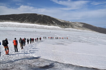 A line of hikers / mountain climbers on an icy glaciar with mountain views in the background