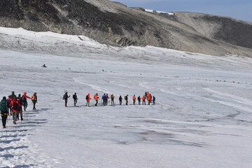 A line of hikers / mountain climbers on an icy glaciar with mountain views in the background