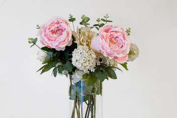 Beautiful arrangement of pink peonies and white blossoms in a clear vase on a light background