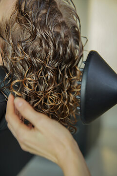 Hairdresser drying brown curly hair with a hair dryer with a diffuser. CGM Curly girl method.