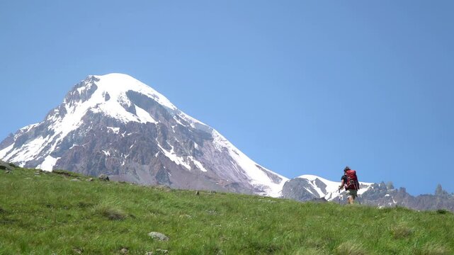 Young Woman Walking Up Mountain Slope With a Backpack. Beautifull High Mountain Peak In The Background