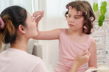 Happiness of Caucasian daughter and Asian mother. Daughter carefully applying blush to mother’s face. Beauty bonding session filled with love and patience. Enjoyable family moment at home.