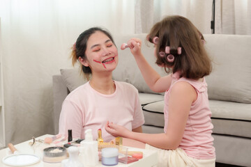 Happiness of Caucasian daughter and Asian mother. Daughter laughing after a playful beauty session. Smiling mother enjoying joyful bonding time. Lighthearted and loving family moment.