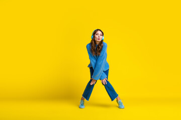 Young woman in blue outfit posing with headphones against bright yellow background