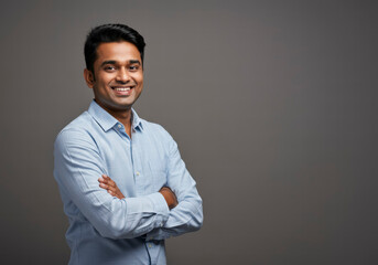 Cheerful Indian Man with Arms Crossed, Exuding Happiness and Professionalism in a Simple Grey Portrait