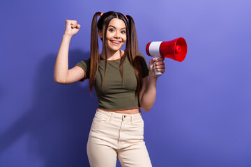 Cheerful young woman with pigtails holding a megaphone against purple wall