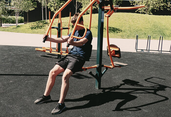 A teenager works out on the outdoor sports ground. He performs strength exercises while sitting on...