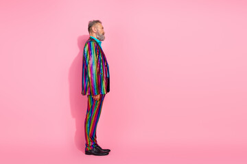 Charismatic elderly man in a shiny colorful striped suit posing against a vibrant pink backdrop conveying an energetic and eccentric style.
