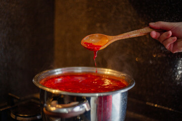 Cooking borscht soup in a pot on a gas stove in the kitchen with wooden spoon