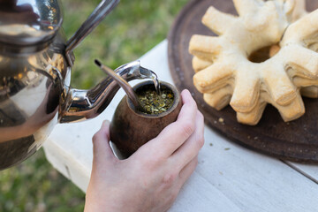 View of a woman's hands preparing yerba mate tea with a kettle, a traditional infusion from Paraguay, Brazil, Argentina and Uruguay, served with hot water with a typical bread for breakfast