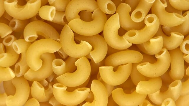 A close-up of vibrant yellow macaroni shells showcases their unique texture, inviting viewers to indulge in the delightful world of pasta. Perfect for food enthusiasts 