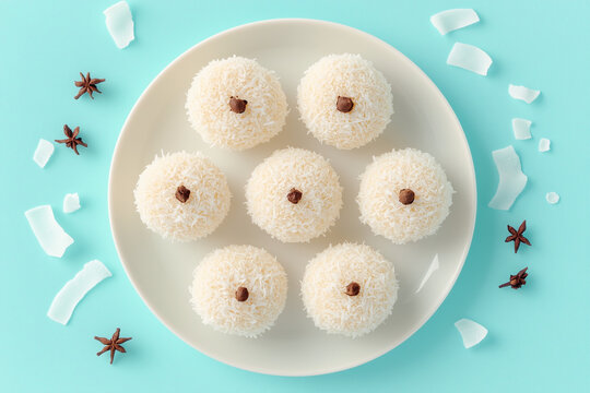 Beijinho coconut sweets with star anise on white plate over blue background