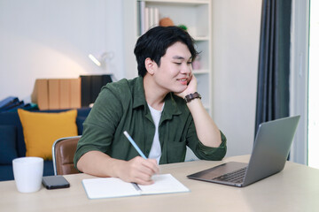 Obraz premium Portrait of home entrepreneur jotting down tasks in notebook on laptop and smiling happily.