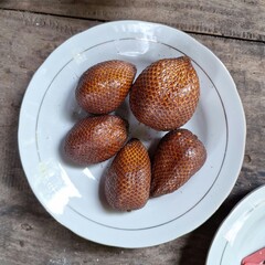 High-Quality Detailed Photo of Salak Fruit (Salacca zalacca) Served on White Plate with Wooden Background – Exotic Tropical Snake Fruit Displayed Elegantly
