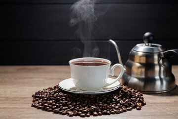 Hot coffee in a white coffee cup With roasted coffee beans on a wooden table, dark black background.