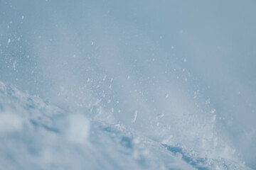Powdery snow drifts and particles fill the air, creating a tranquil and picturesque wintry scene. Capturing the purity and peacefulness of winter showcases the delicate movement of snow under a vivid