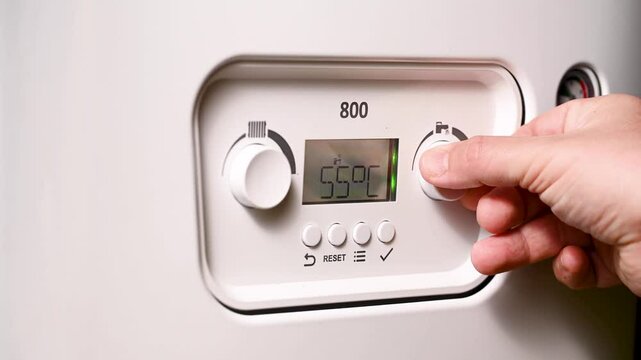 Men hand setting temperature button on control panel of central heating at combi boiler. Incressing price for gas