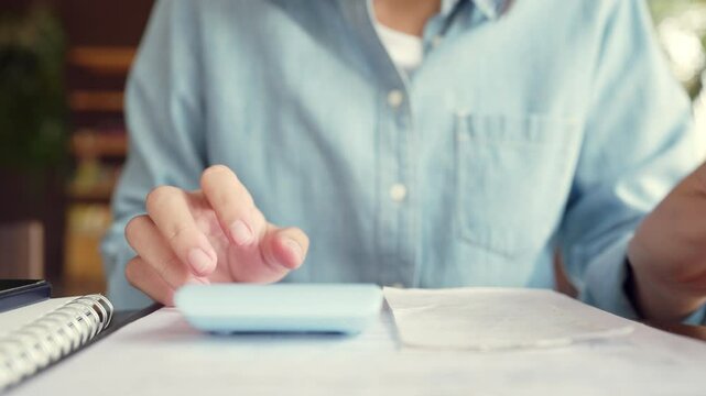 A woman is using a calculator to add up the cost of her purchases. She is focused on the task at hand and she is in a serious mood