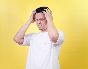 An asian man shows frustration while holding his head, against a bright yellow background