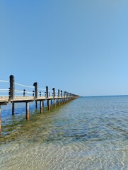 Fototapeta premium long pontoon bridge extending into the sea, open sea, sea coast, deserted beach without people, bridge on piles