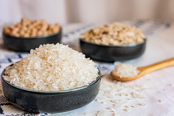 Close-up of a bowl filled with white rice, with scattered grains and a wooden spoon in the background, creating a soft and natural kitchen scene