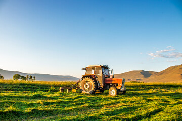 A vintage tractor in a sunny field with a mountain backdrop in Erzurum, Turkey.