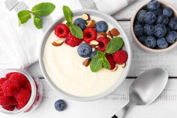 Tasty cooked semolina porridge with almonds, berries and mint on white wooden table, top view