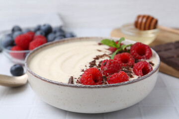 Tasty cooked semolina porridge with raspberries, chocolate and mint on white table, closeup