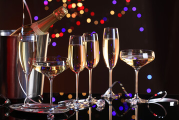 Champagne in glasses and ice bucket with bottle on mirror surface against dark background with blurred lights