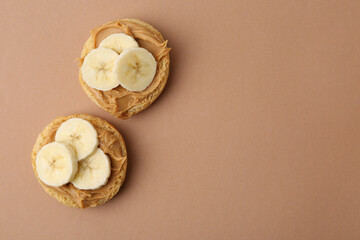 Tasty sandwiches with peanut butter and banana on brown background, top view. Space for text
