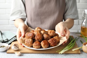 Woman holding plate with delicious meatballs at light textured table, closeup