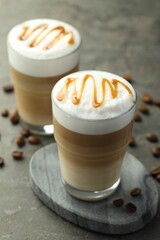 Tasty latte macchiato in glasses and coffee beans on grey table, closeup