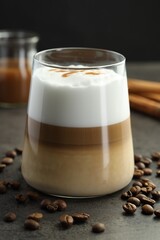 Tasty latte macchiato in glass, coffee beans and cinnamon on grey table, closeup