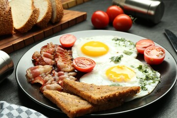 Tasty brunch. Delicious fried eggs, bacon and pieces of toast served on black table, closeup