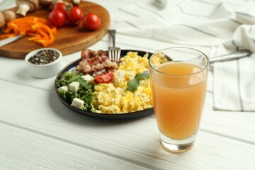 Tasty brunch. Glass of apple juice and scrambled eggs with bacon served on white wooden table, closeup